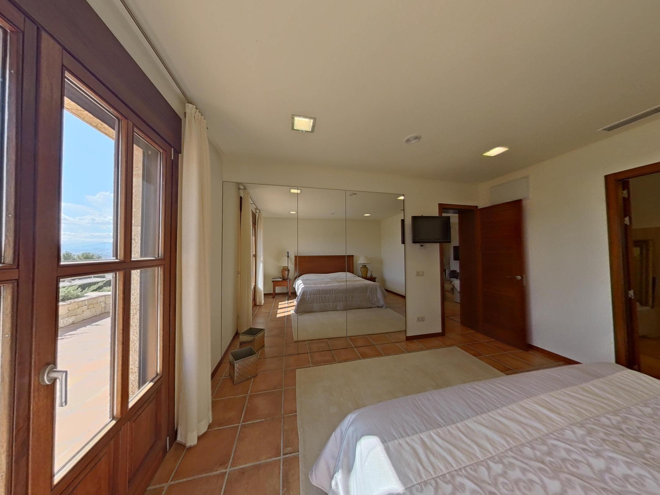 Bedroom with terracotta flooring, mirrored built-in wardrobes, and natural light from wooden-framed doors leading to a terrace.