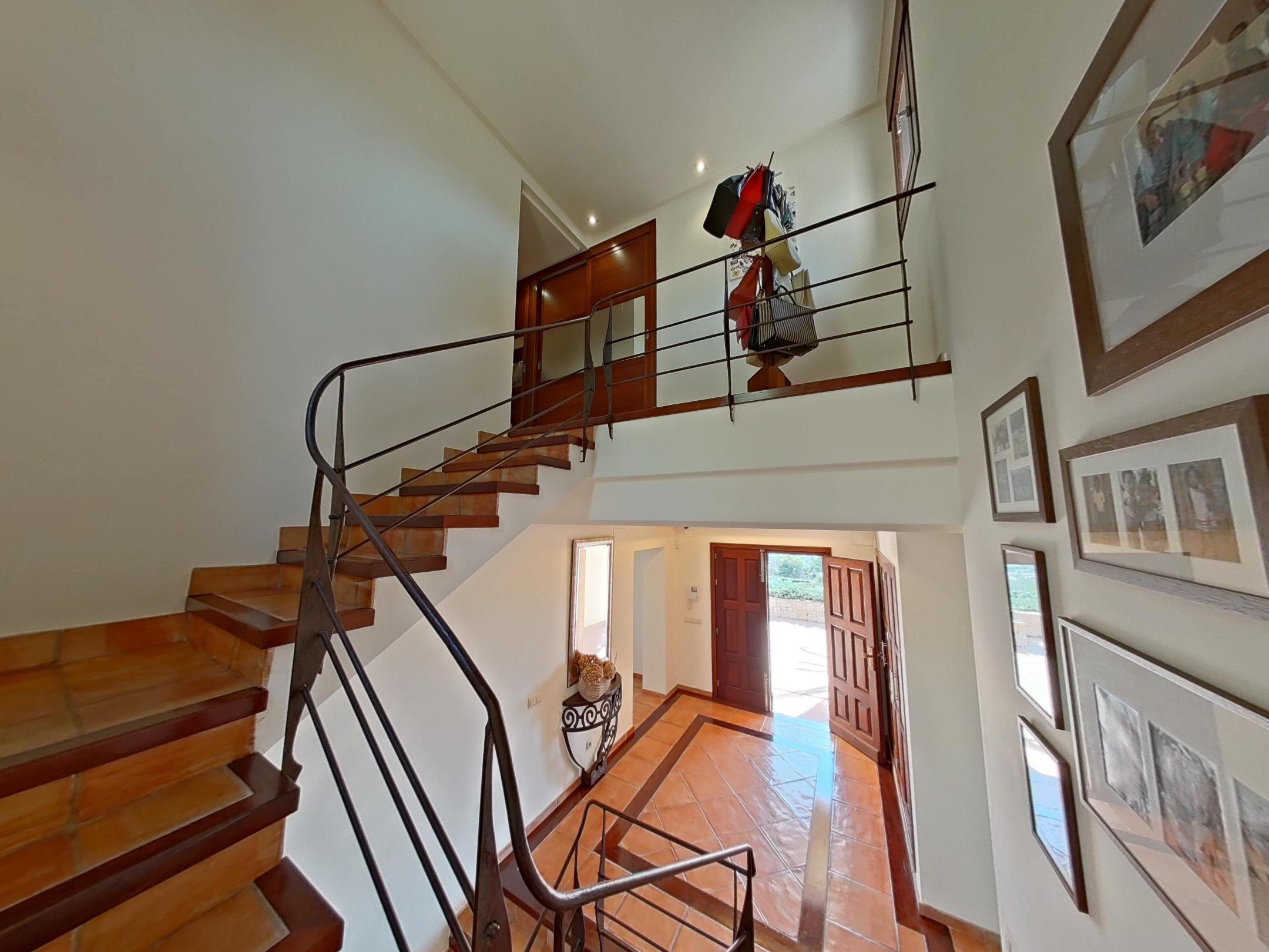 Entrance hall viewed from the staircase, featuring terracotta tile flooring with decorative borders, a wrought iron railing, and wooden double doors.