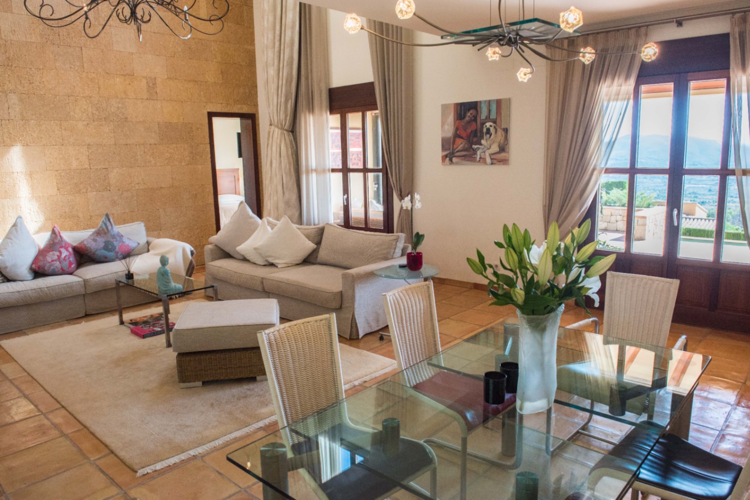Open-plan living and dining area featuring a textured stone wall, terracotta tile flooring, and large glass doors providing abundant natural light.
