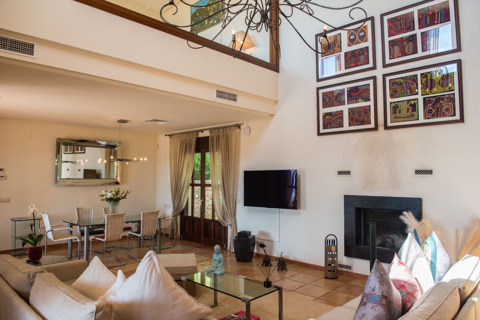 Spacious living area with terracotta floors, featuring a double-height ceiling, a black-framed fireplace, and a dining zone with a glass table and rattan chairs.