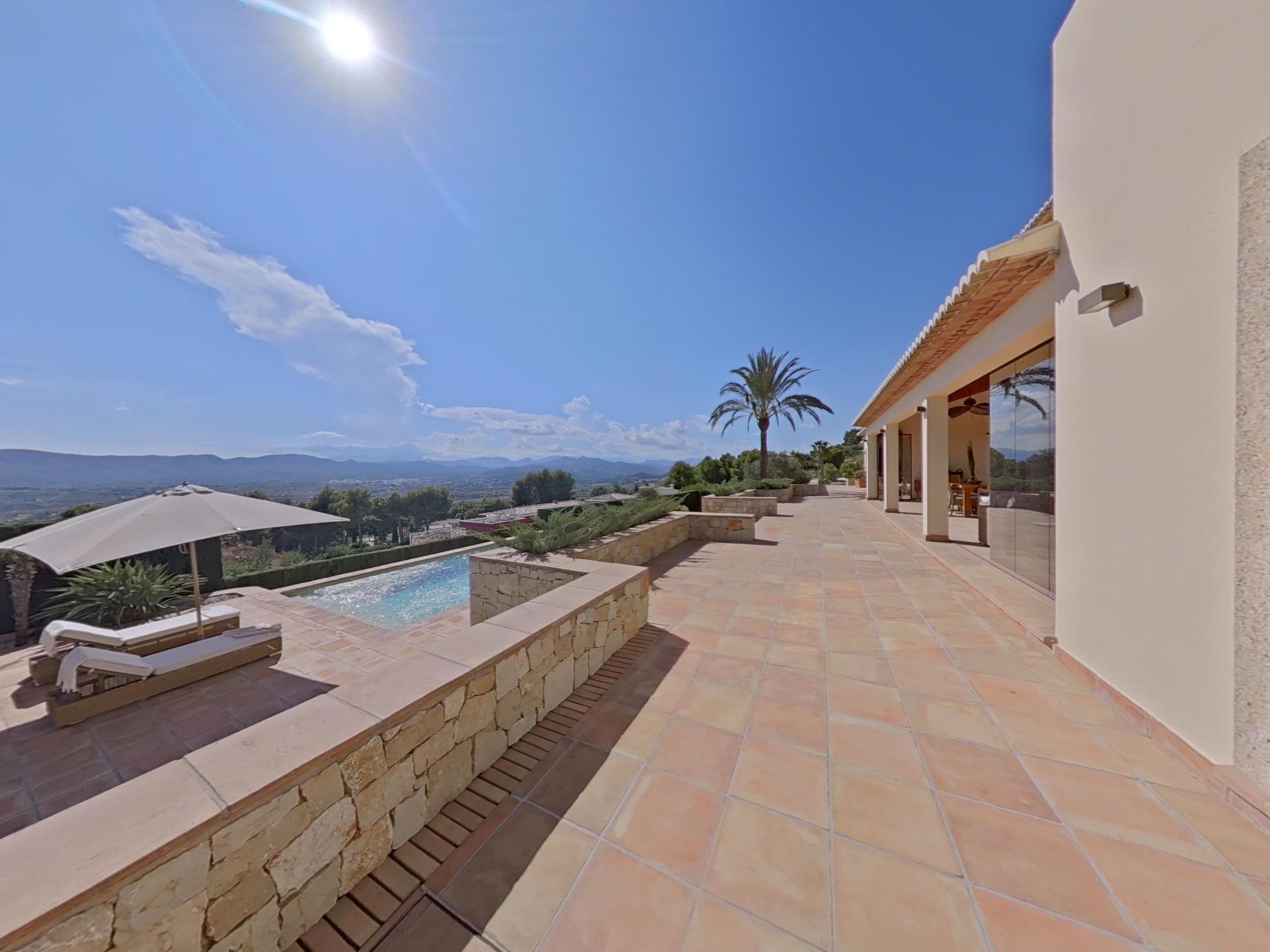 Wide terrace with terracotta tiles, stone retaining walls, and a pool area overlooking a panoramic valley and mountain landscape.
