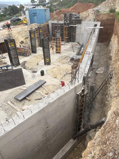 Foundation phase showing reinforced concrete retaining walls and vertical formwork for structural columns on an excavated construction site.