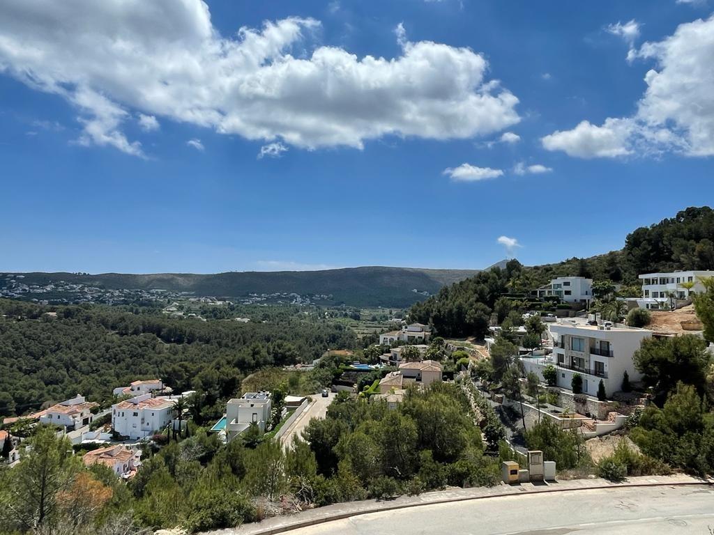 Elevated view of a Mediterranean valley featuring white villas nestled among dense pine forests under a bright sky.