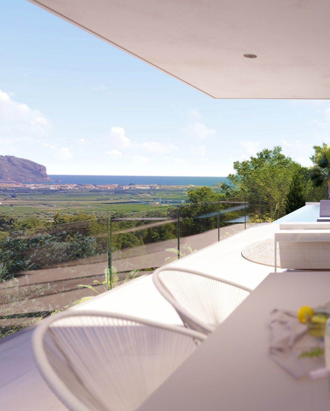 Elevated terrace with glass balustrades offering panoramic views of the Mediterranean coast and distant mountains. Features modern cord seating and a white dining area.