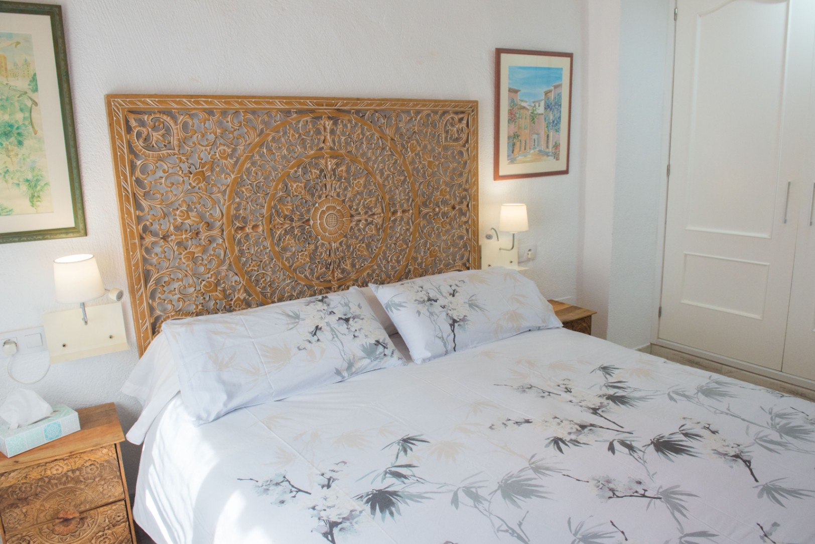 Bedroom featuring a hand-carved wooden headboard with intricate mandala patterns, matching nightstands, and integrated wall lighting.