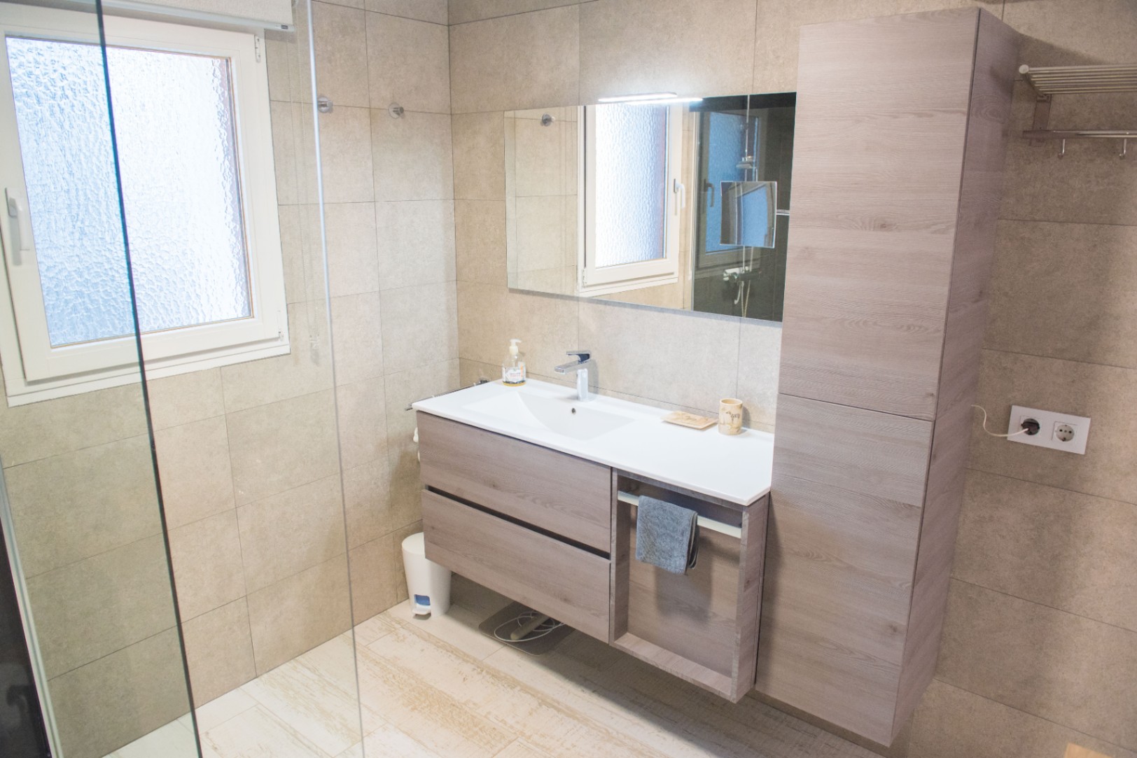 Modern bathroom featuring a floating wood-grain vanity with integrated sink, matching tall storage cabinet, and large-format sand-colored wall tiles.