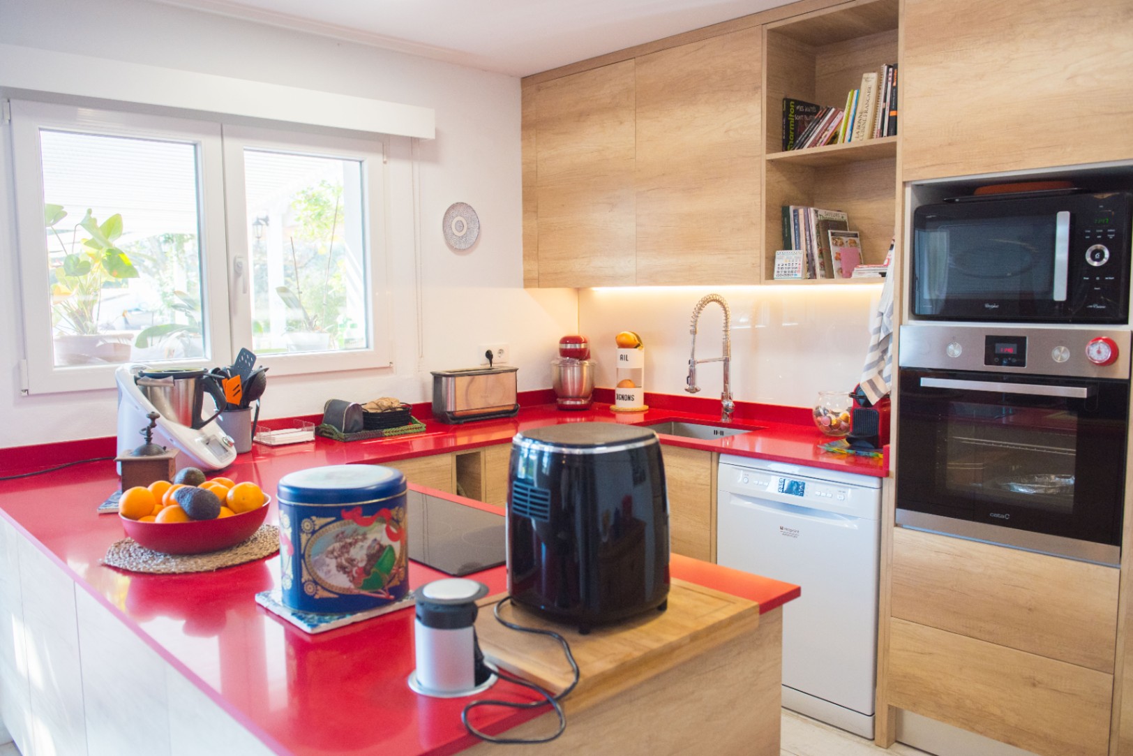Modern kitchen featuring a vibrant red countertop, light wood cabinetry, and integrated appliances including a built-in oven, microwave, and dishwasher.