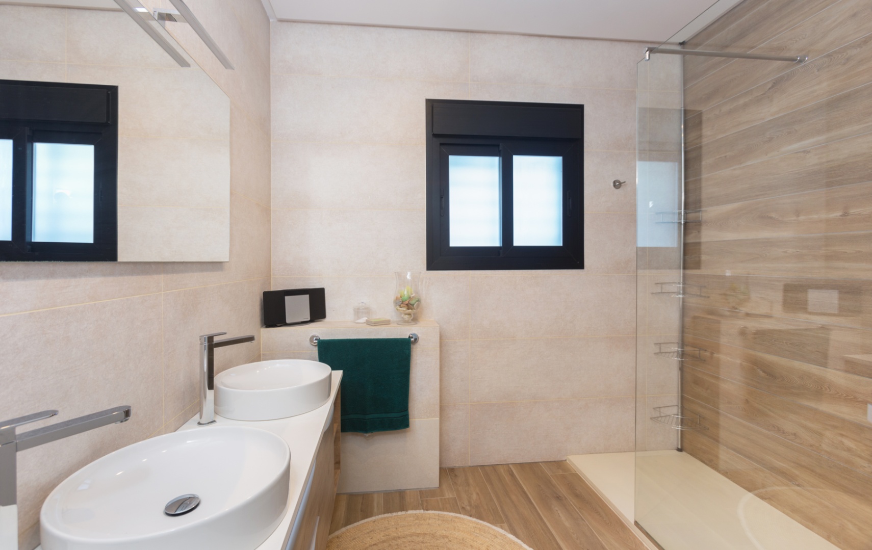 Modern bathroom featuring a double vessel sink vanity, wood-effect floor and wall tiling, and a walk-in shower with a glass screen and black-framed window.
