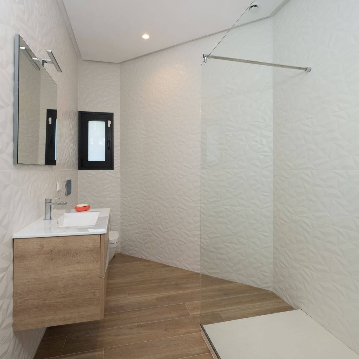 Modern bathroom featuring textured geometric wall tiles, a floating light wood vanity, and a walk-in shower with a frameless glass screen.