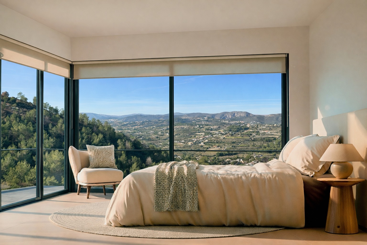 Bedroom with floor-to-ceiling corner windows offering panoramic valley and mountain views. Features neutral tones, a wooden side table, and natural light.