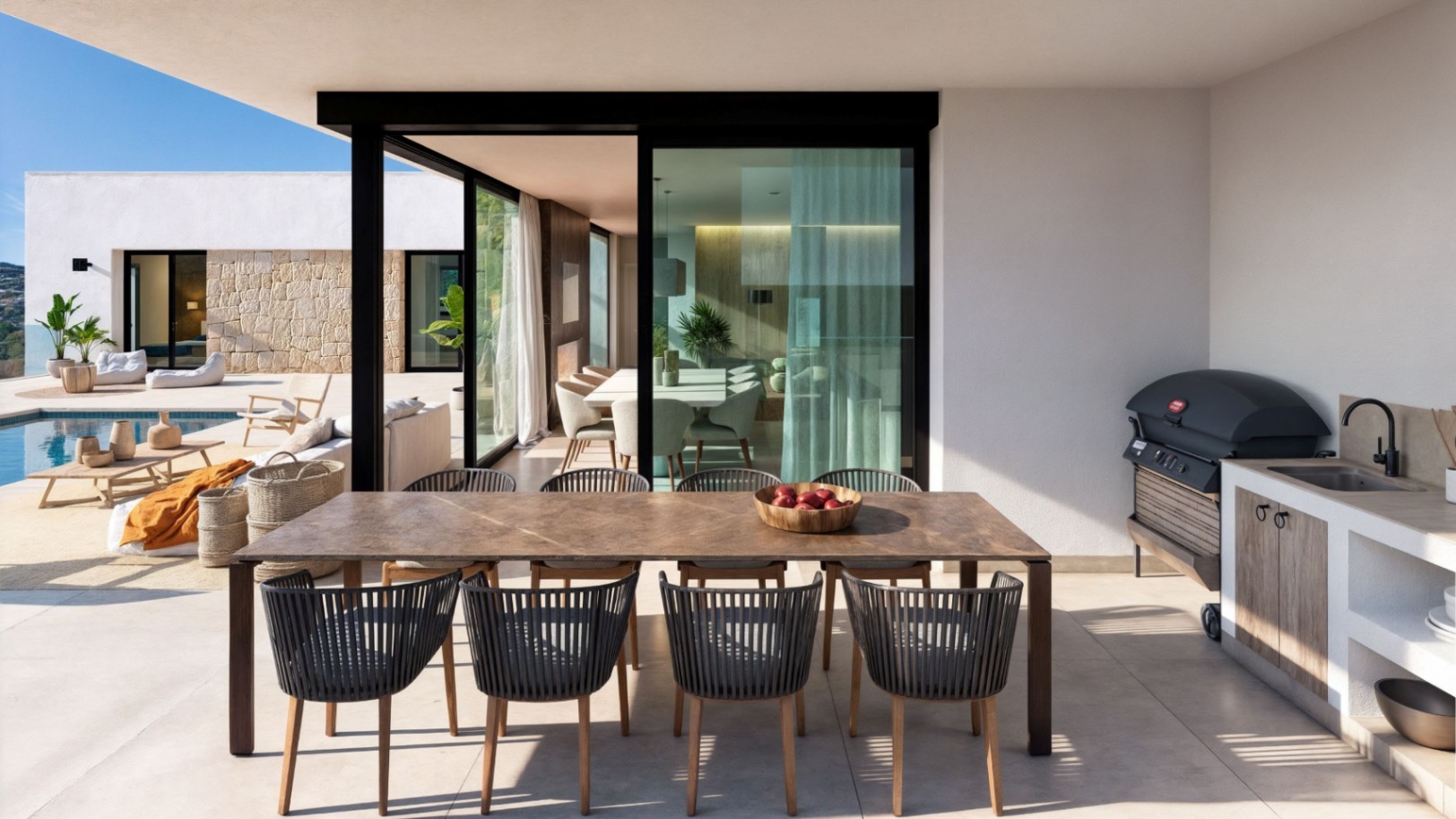 Covered outdoor terrace featuring a large wooden dining table, modern rope chairs, and a fully equipped outdoor kitchen with a grill and sink overlooking the pool.