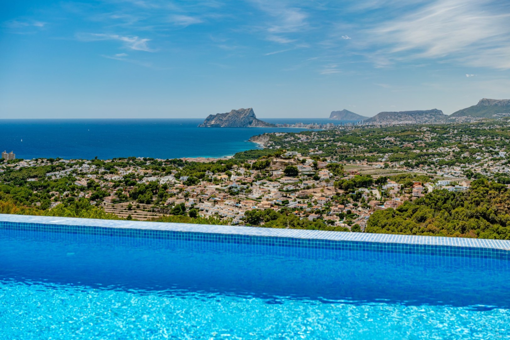 Infinity pool with blue mosaic tiling overlooking a panoramic coastal view of the Mediterranean, featuring the Peñón de Ifach and the Calpe skyline.