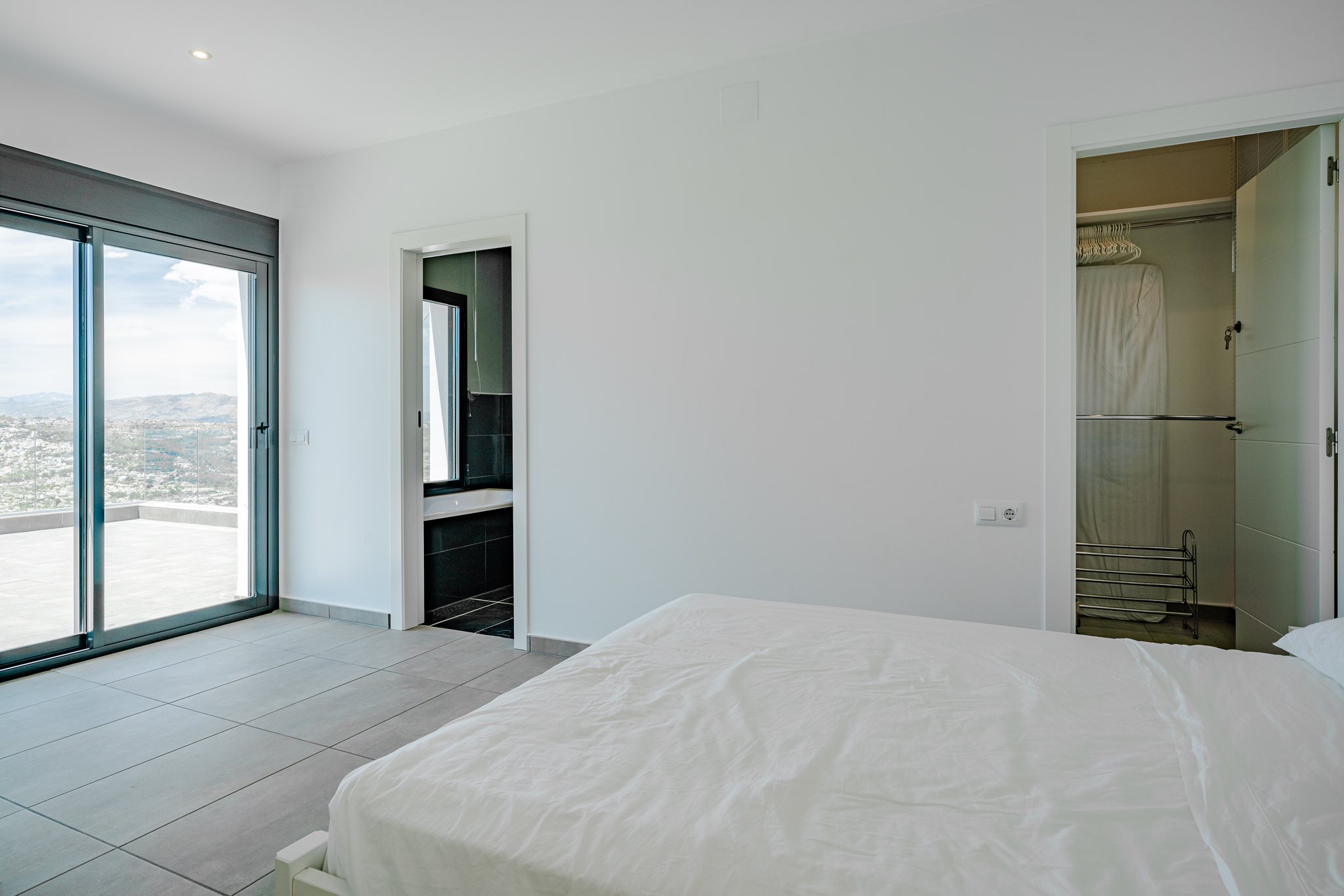 Modern bedroom featuring a large sliding glass door to a terrace, an en-suite bathroom with dark tiling, and a functional walk-in closet.