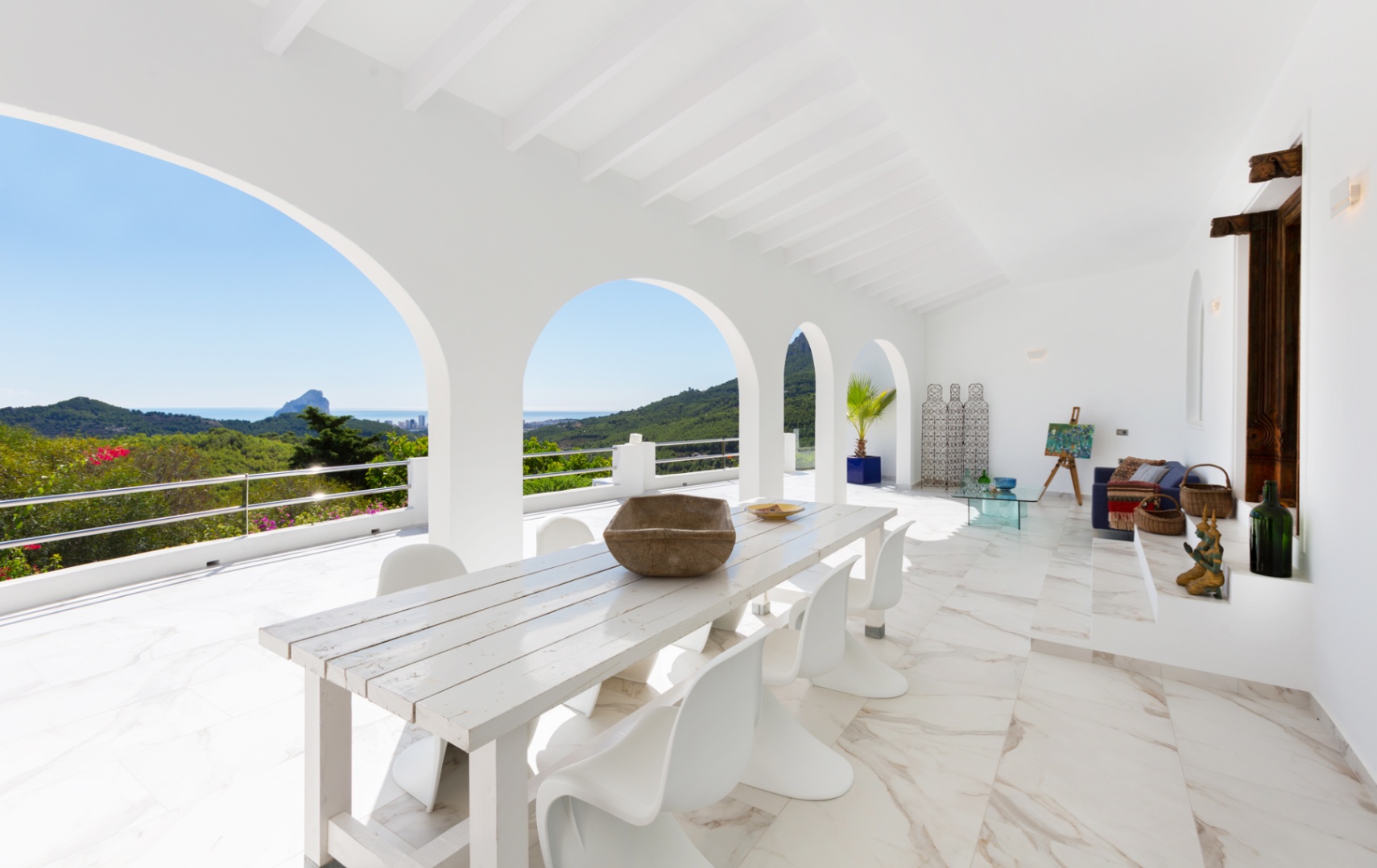 Covered terrace featuring white arches, marble-effect flooring, and a dining area with panoramic views of the Mediterranean coastline and Peñón de Ifach.