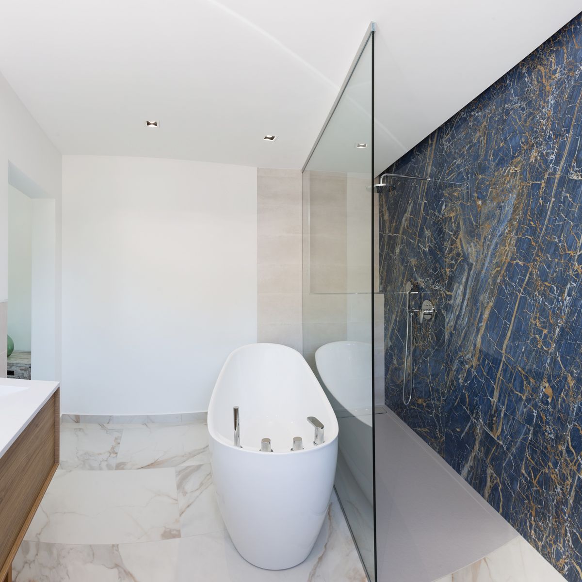Modern bathroom featuring a freestanding oval bathtub, walk-in shower with a blue marble feature wall, and white marble flooring with gold veining.