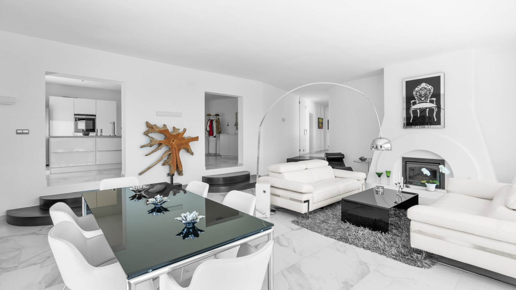 Open-plan living area featuring marble flooring, white leather sofas, a modern fireplace, and a glass dining table with views into the minimalist kitchen.