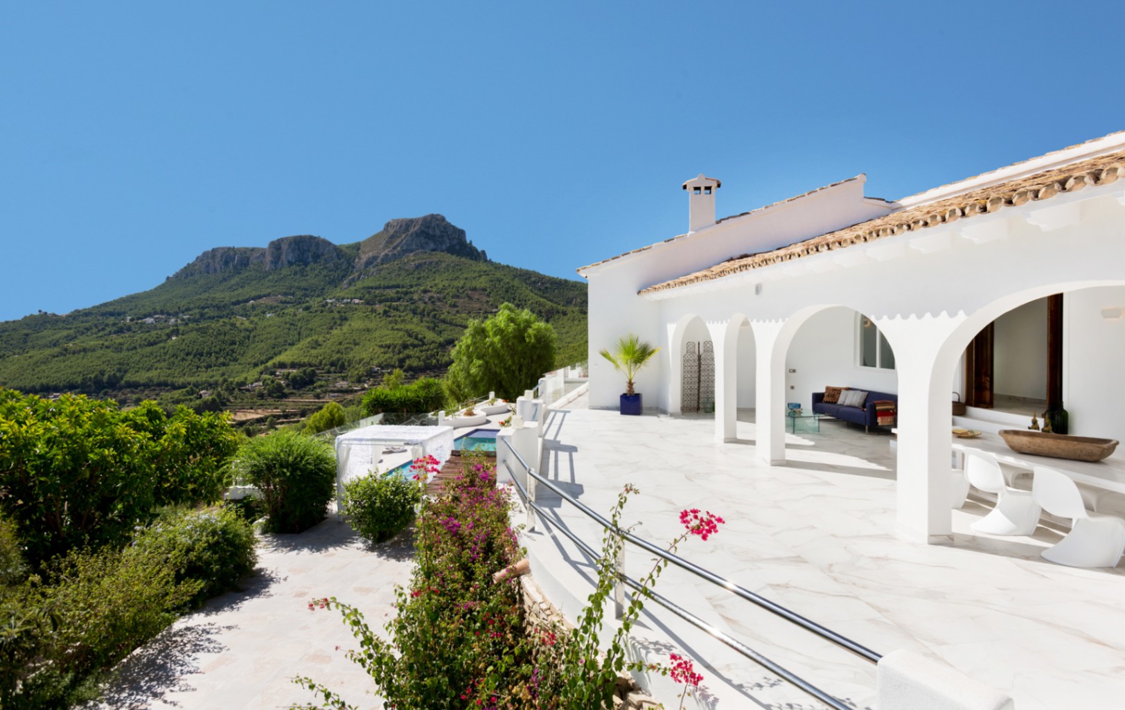 White Mediterranean villa featuring an arched terrace with marble flooring, outdoor lounge area, and expansive views of the lush mountain landscape.