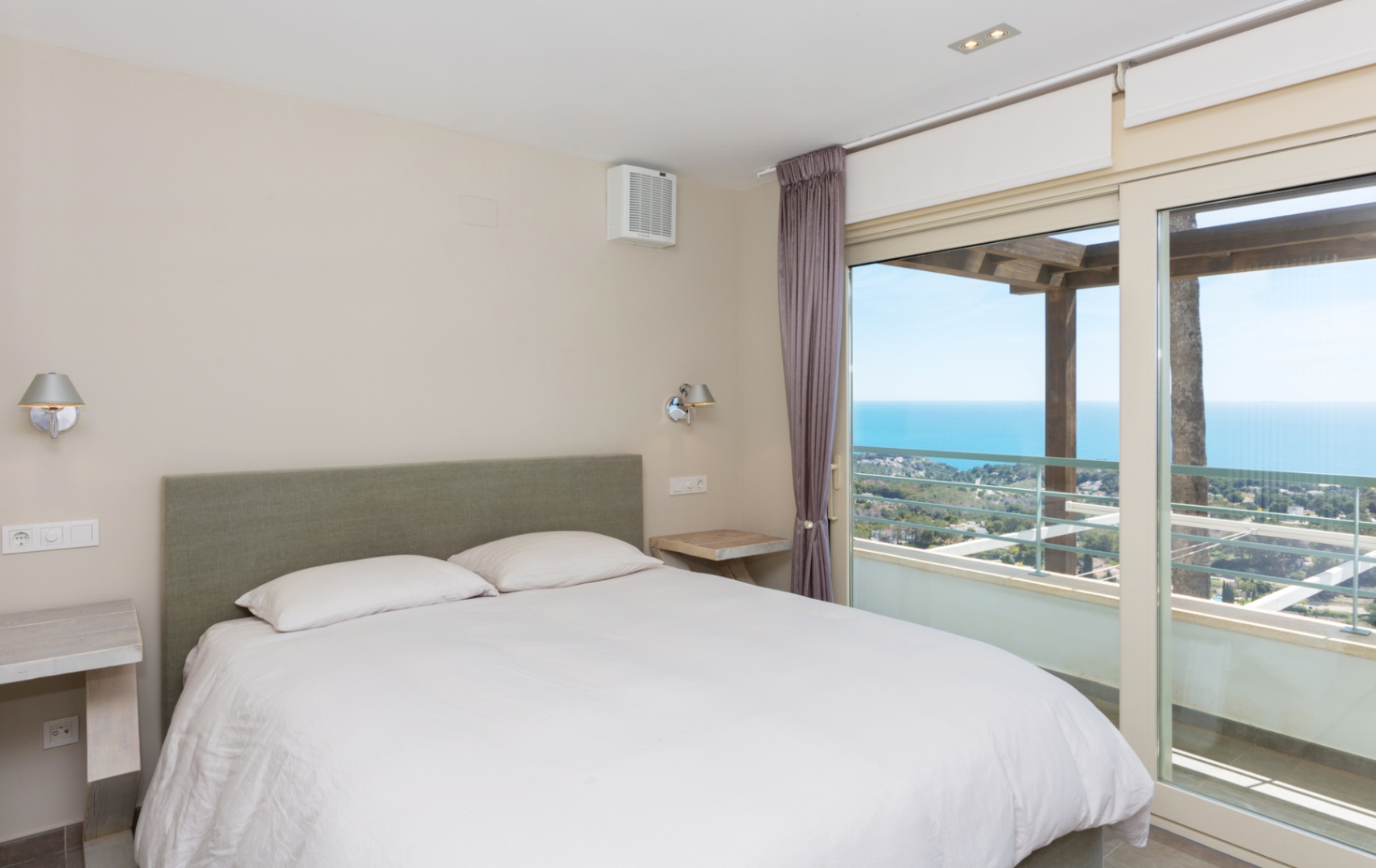 Bedroom featuring a green upholstered headboard and large sliding glass doors that open onto a terrace with a wooden pergola and panoramic sea views.