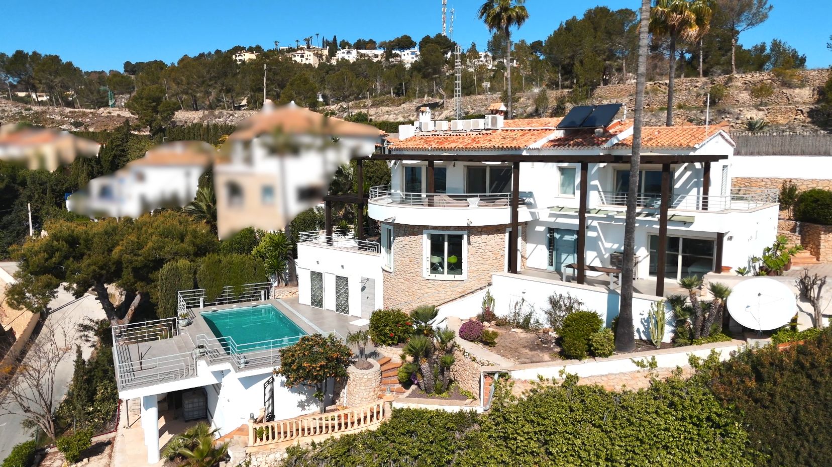 Multi-level villa with white facade, stone detailing, solar panels, and a rectangular swimming pool set within Mediterranean landscaping and palm trees.