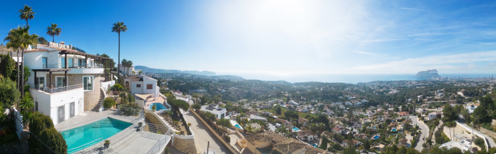 Panoramic view of a multi-level Mediterranean villa featuring a private pool, stone-clad walls, and expansive terraces overlooking the coastline and Peñón de Ifach.
