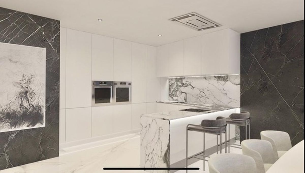 Modern kitchen featuring minimalist white cabinetry, a marble waterfall island, integrated double ovens, and dark marble wall panels with recessed lighting.