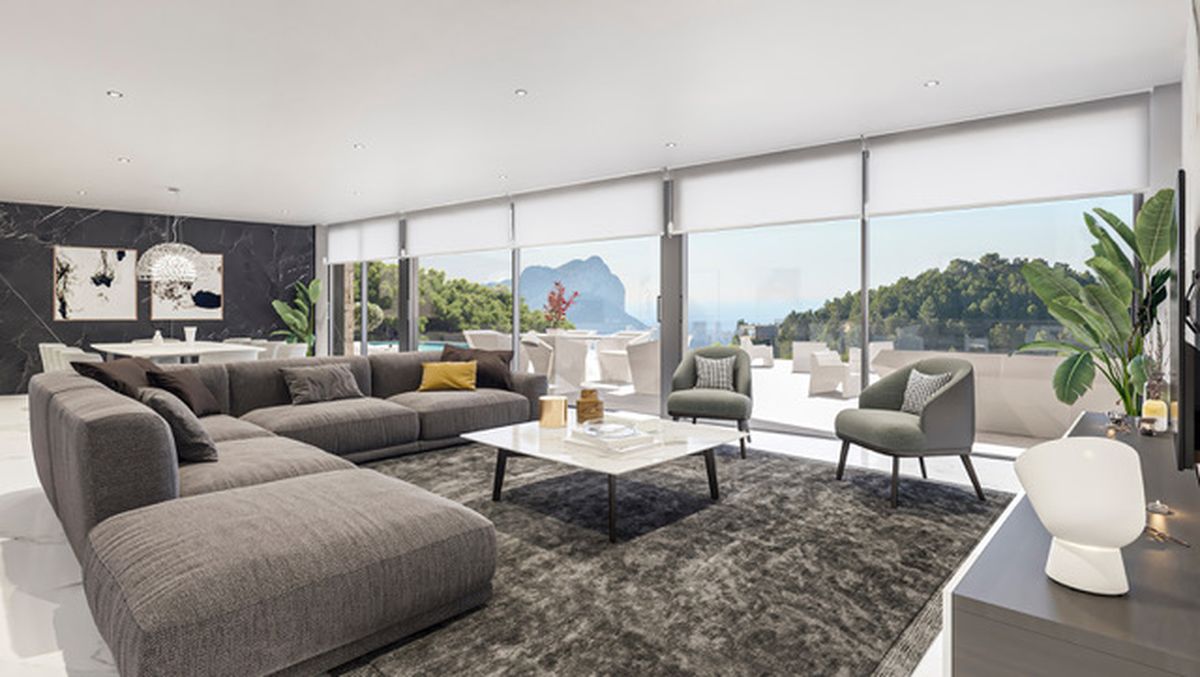 Spacious living area with a grey sectional, marble table, and floor-to-ceiling windows showcasing views of the Peñón de Ifach and the Mediterranean coast.