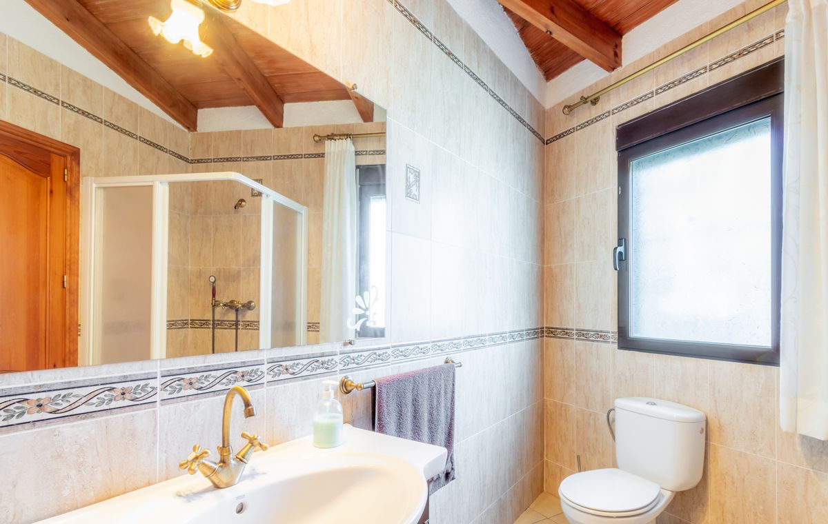 Bathroom featuring a sloped wooden ceiling with exposed beams, beige tiling with decorative borders, and classic brass fixtures.