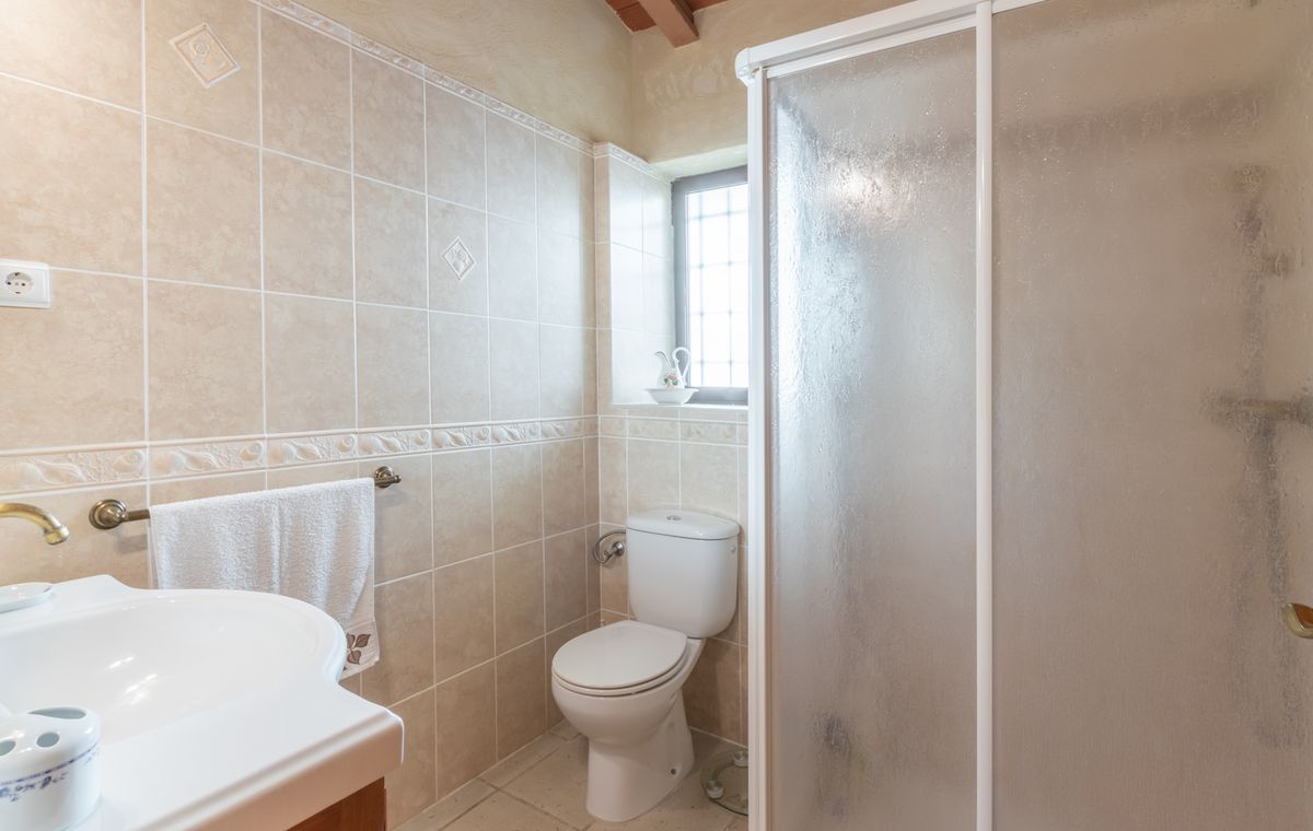 Bathroom featuring beige ceramic wall tiles with decorative borders, a white toilet, and a shower enclosure with frosted glass doors under exposed wooden beams.