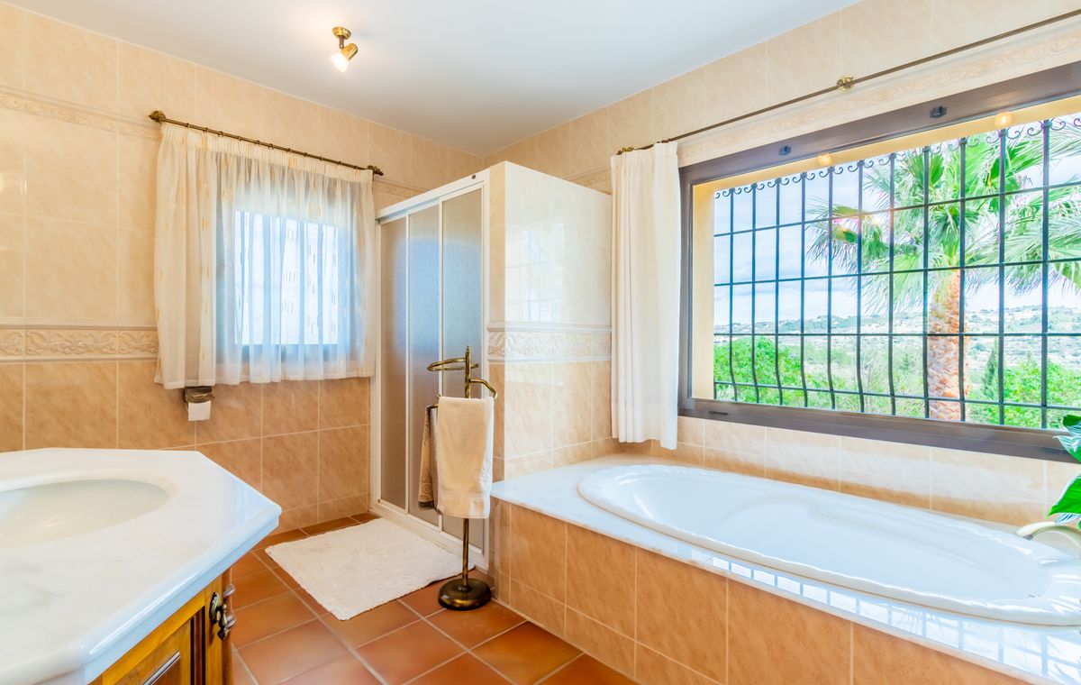 Bathroom with a built-in bathtub under a window, separate shower cabin, white marble vanity, and rustic terracotta floor tiles.