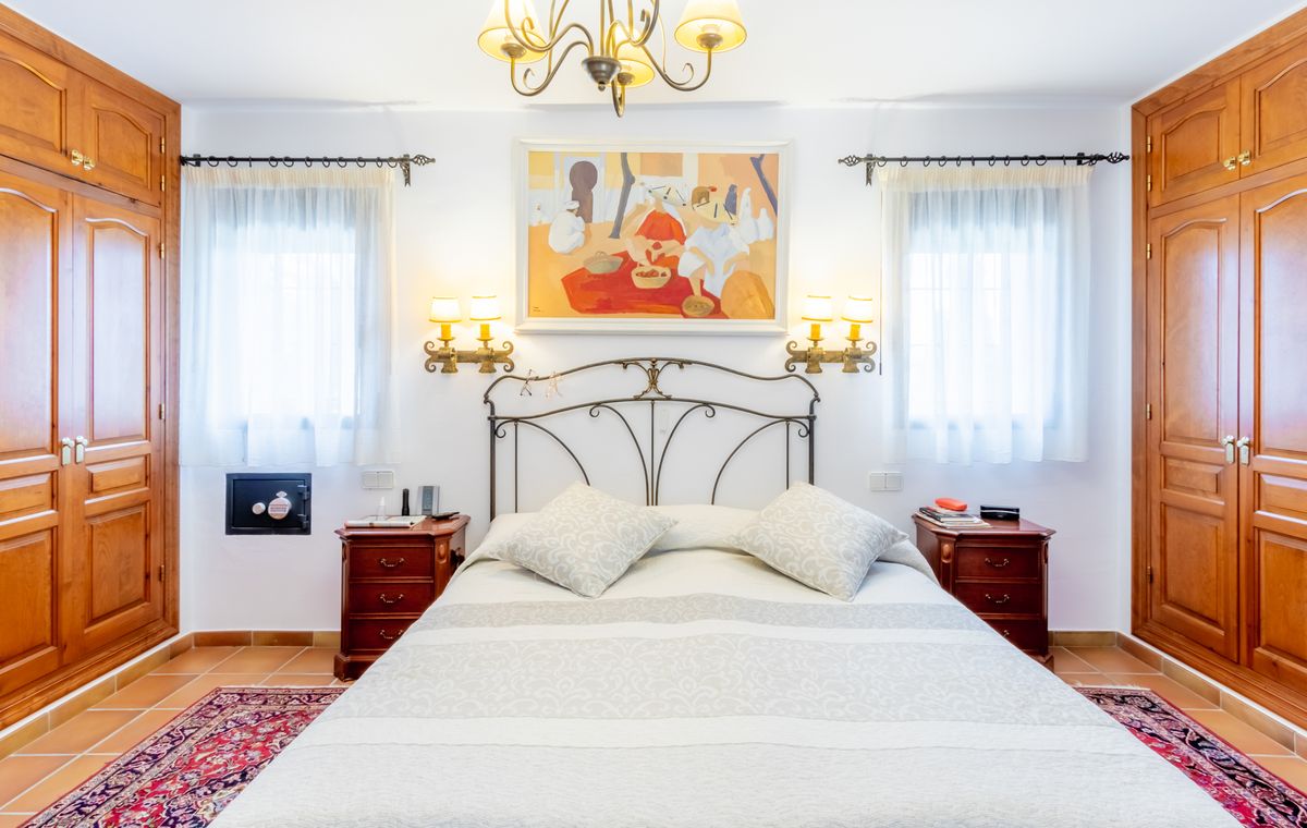 Bedroom featuring a wrought iron headboard, symmetrical wooden built-in wardrobes, and terracotta tile floors. Includes wall-mounted sconces and a built-in safe.