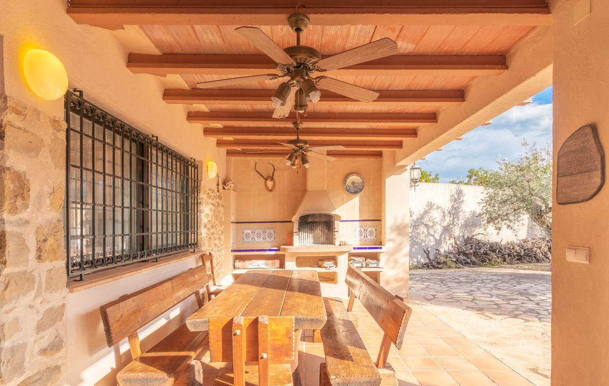 Covered terrace featuring a wooden beamed ceiling with fans, a large rustic dining set, and a built-in barbecue with decorative tiling and stone accents.