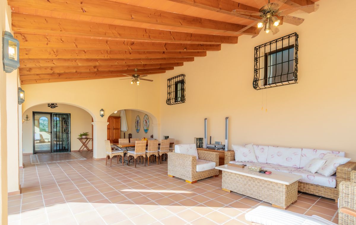 Covered terrace featuring an exposed wooden beam ceiling, terracotta tile flooring, and a lounge area with wicker furniture and a dining set.