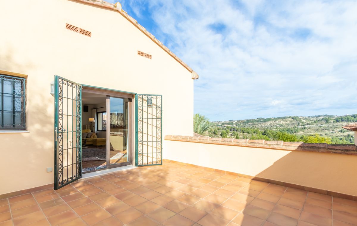 Elevated terrace with terracotta tiles and green wrought iron gates, offering panoramic views over the green valley and surrounding hills.