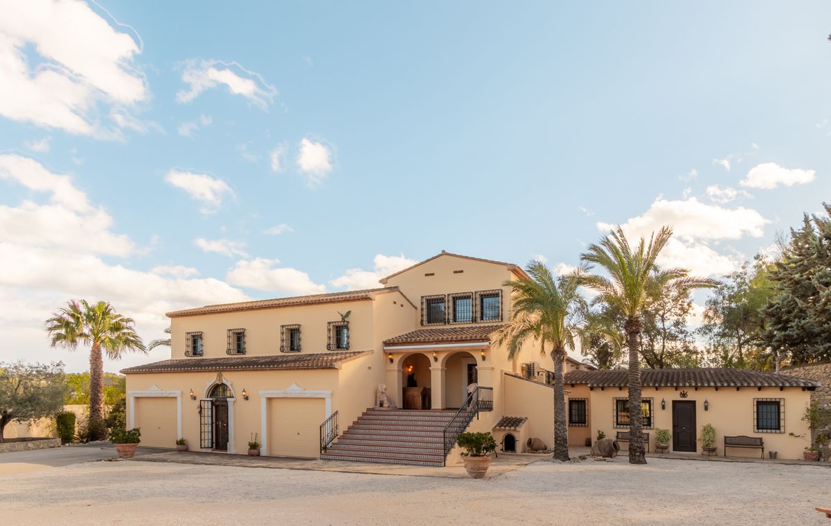 Exterior view of a Mediterranean villa featuring a cream facade, terracotta roof, wide tiled staircase leading to an arched porch, and integrated garages.
