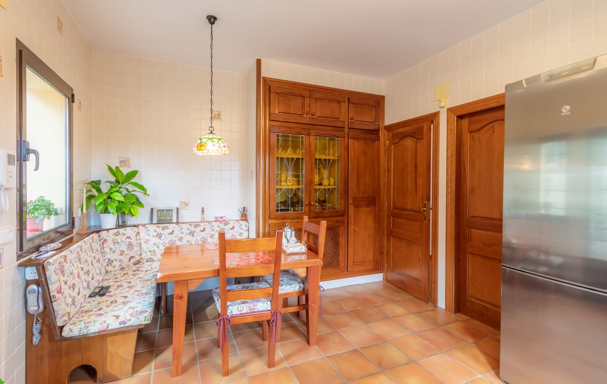 Kitchen dining area featuring a built-in wooden bench with floral upholstery, terracotta flooring, and custom cabinetry with glass displays.