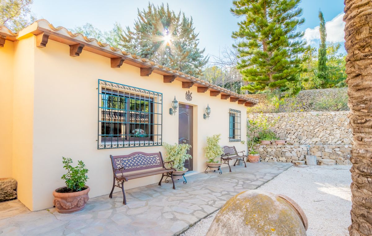 Mediterranean villa exterior featuring a cream facade, terracotta roof tiles with wooden beams, and windows with decorative wrought iron grilles.