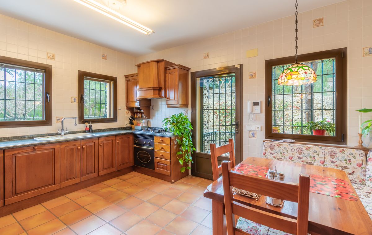 Rustic kitchen featuring dark wood cabinetry, terracotta tile flooring, and a dining nook with a Tiffany-style pendant lamp and floral bench seating.