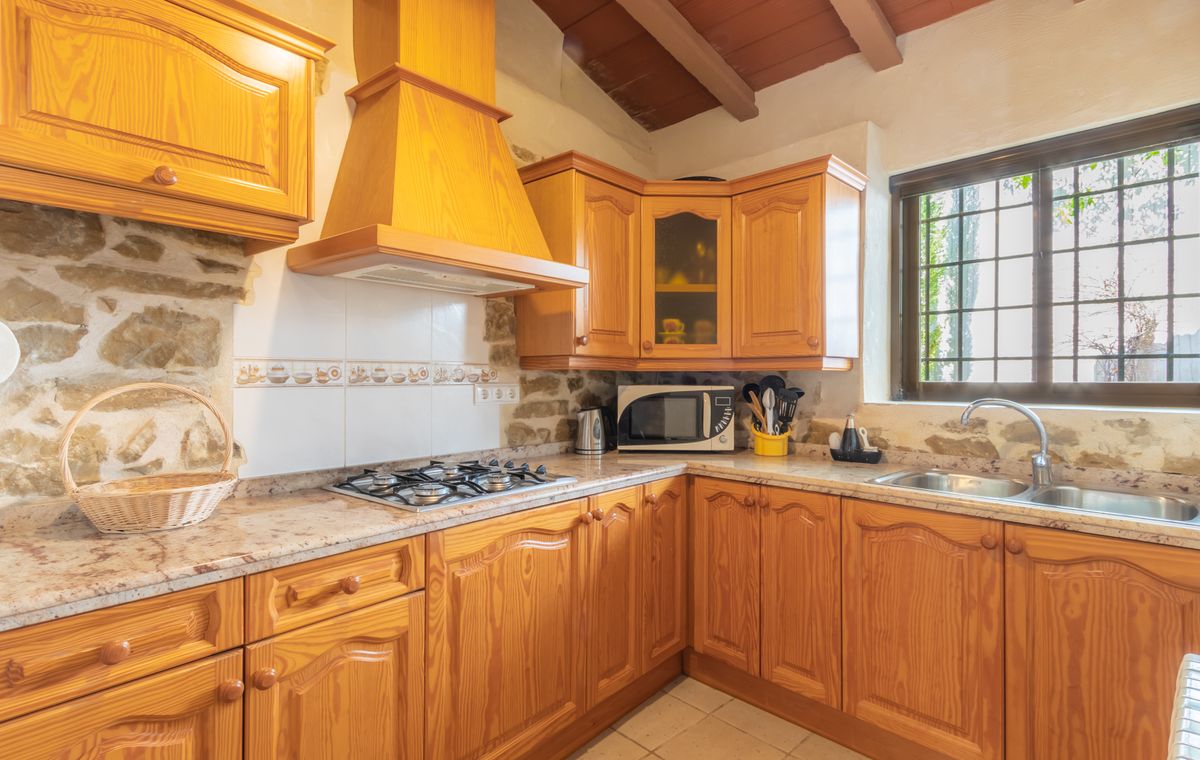 Rustic kitchen featuring honey-toned wooden cabinetry, exposed stone walls, and a granite countertop. Includes a gas cooktop, matching range hood, and beamed ceiling.