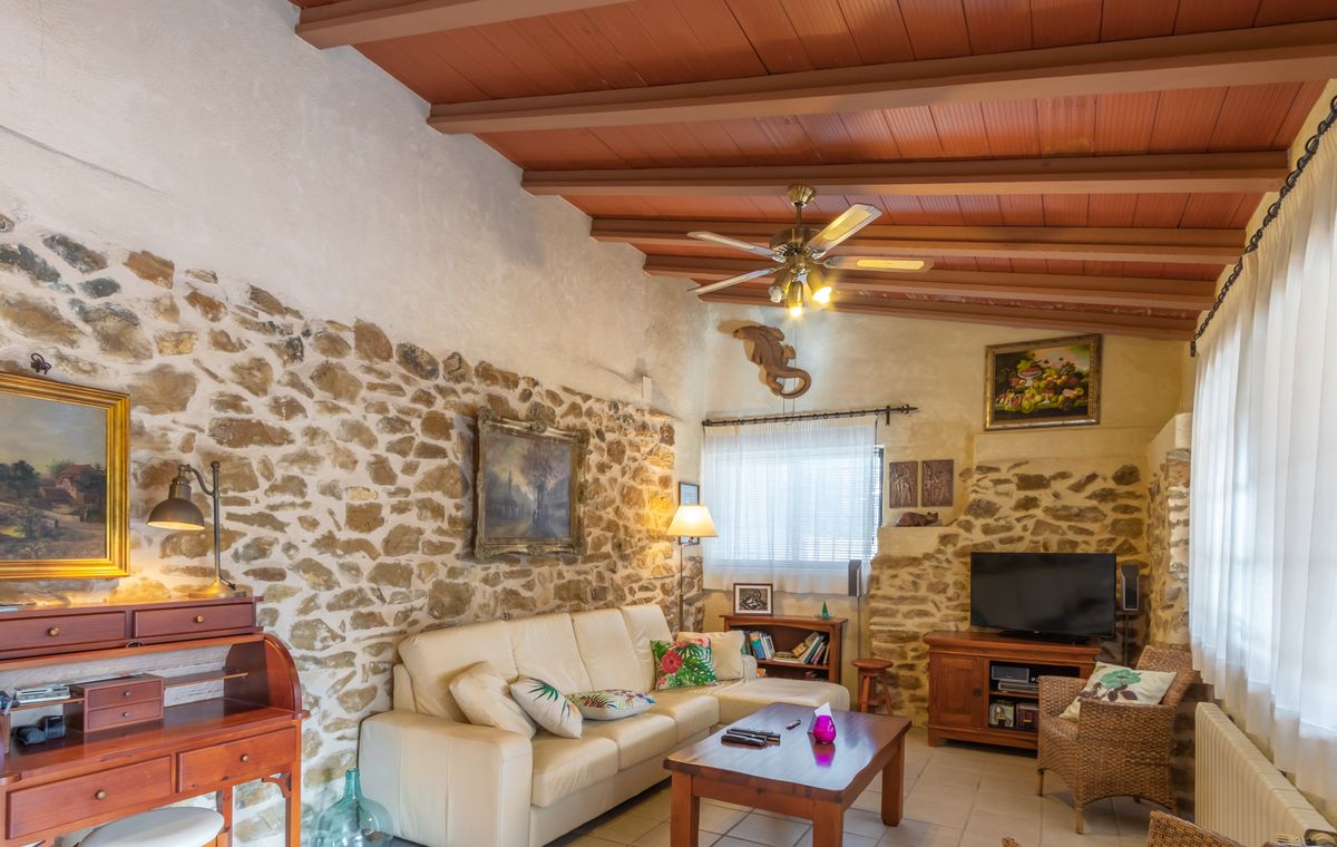 Rustic living area featuring exposed stone walls, a beamed wooden ceiling, and a cream leather sofa complemented by a traditional roll-top desk.