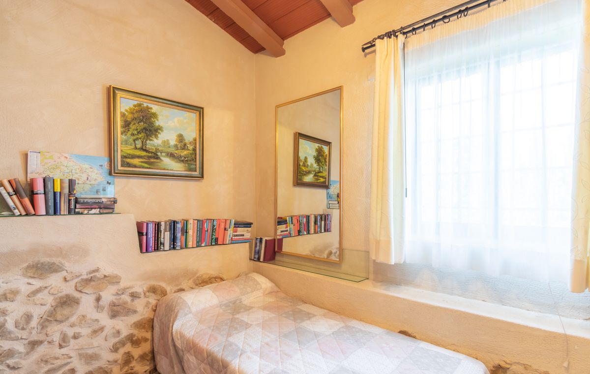 Small bedroom featuring a single bed, exposed wooden ceiling beams, and a rustic stone wall detail. Includes integrated glass bookshelves and a large vertical mirror.