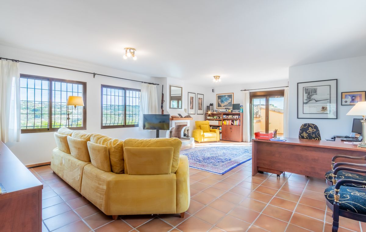 Spacious living area featuring terracotta flooring, a large yellow sectional sofa, a dedicated workspace with a wooden desk, and a fireplace.
