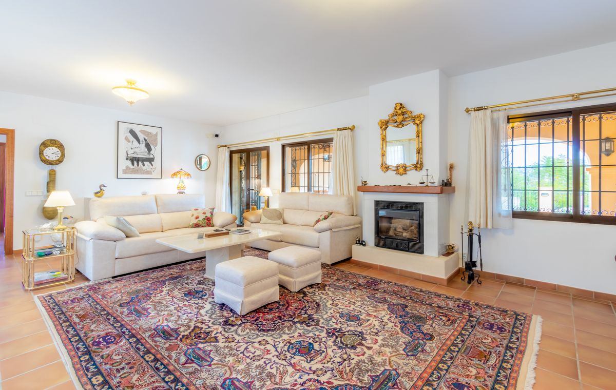 Spacious living room featuring terracotta flooring, a classic fireplace with an ornate gold mirror, and white sofas centered around a large patterned rug.