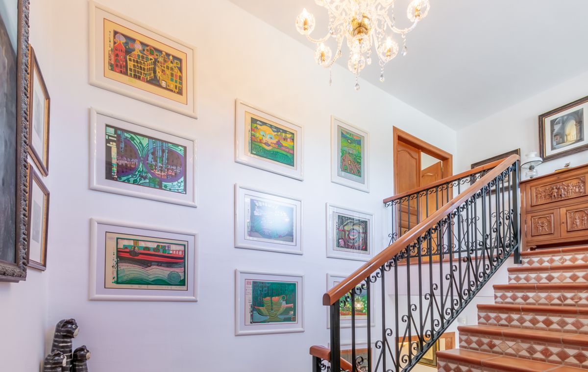 Staircase featuring terracotta tiles with patterned risers, a wrought iron railing, and a gallery wall of framed artwork illuminated by a crystal chandelier.