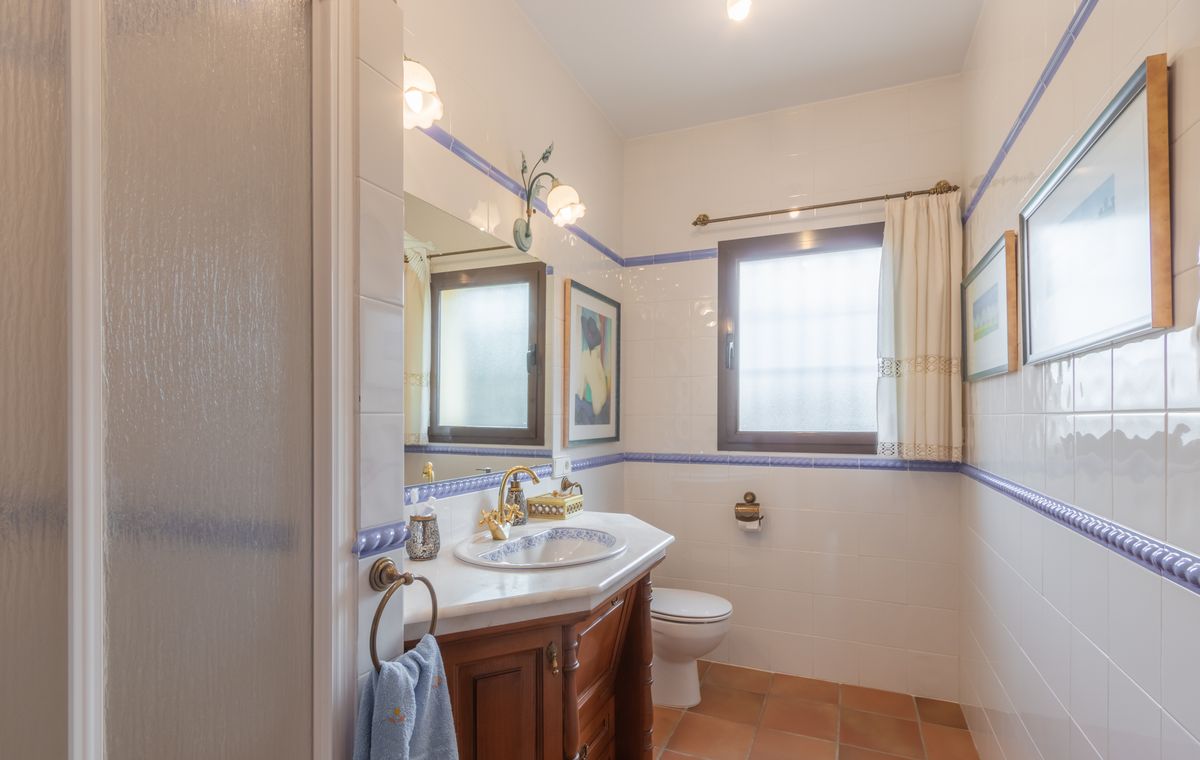Traditional bathroom featuring white wall tiles with blue borders, a wooden vanity with marble top, and rustic terracotta floor tiles.