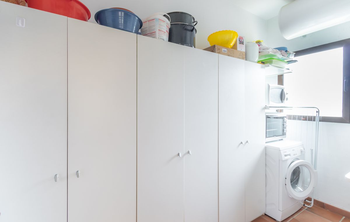 Utility room featuring extensive white storage cabinetry, terracotta flooring, and a laundry area with a washing machine and stacked appliances.