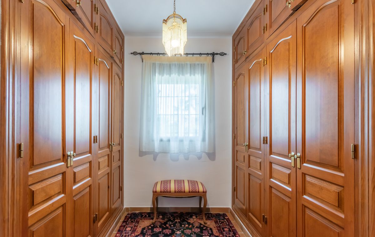 Walk-in closet featuring floor-to-ceiling wooden wardrobes, a decorative chandelier, and a central window.