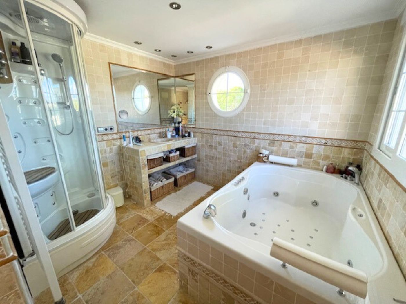 Bathroom featuring a hydromassage bathtub, a curved glass shower cabin, and tiled walls with a distinctive circular porthole window.