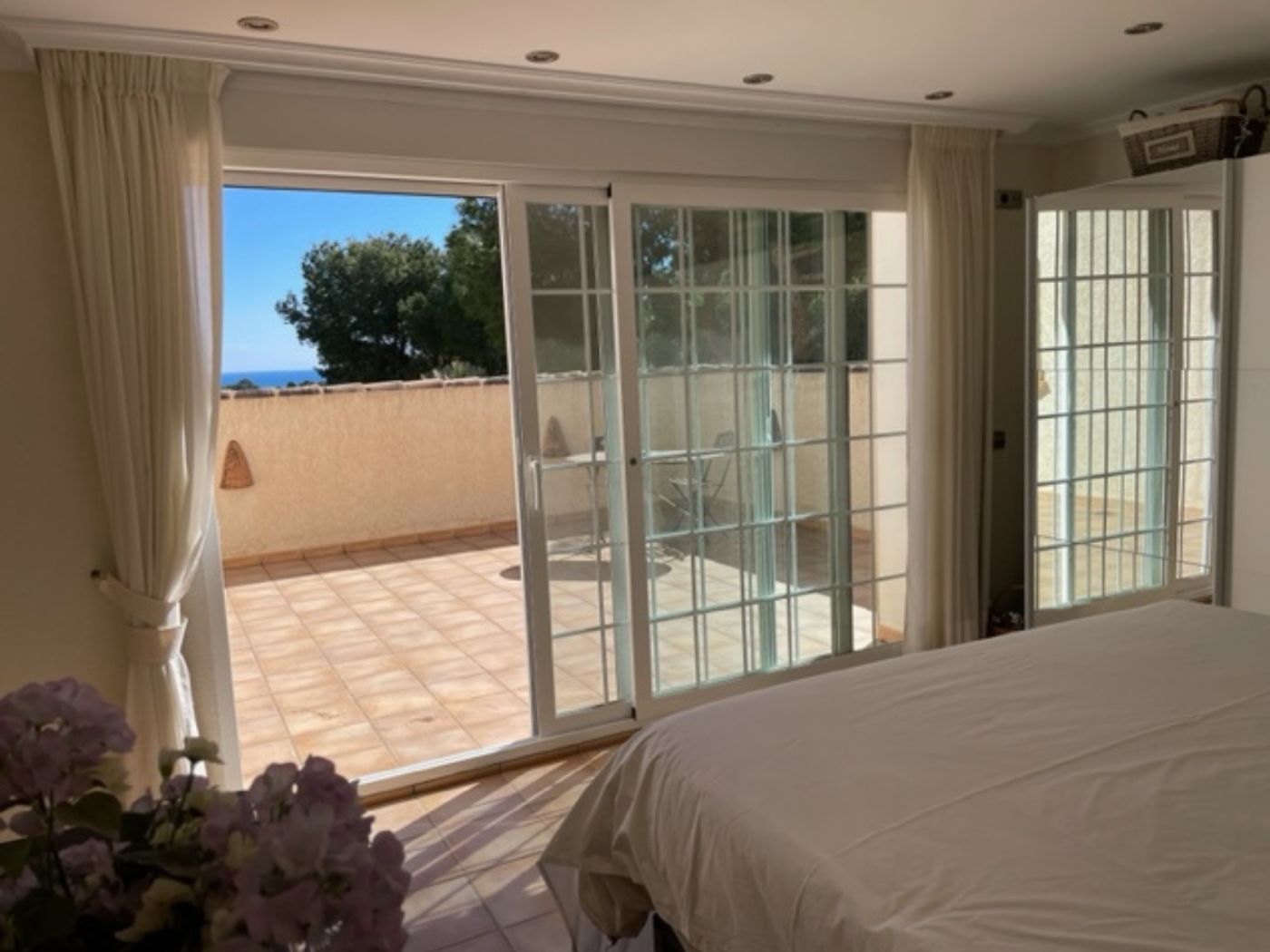 Bedroom featuring large sliding glass doors that open onto a private tiled terrace with sea views and outdoor seating.