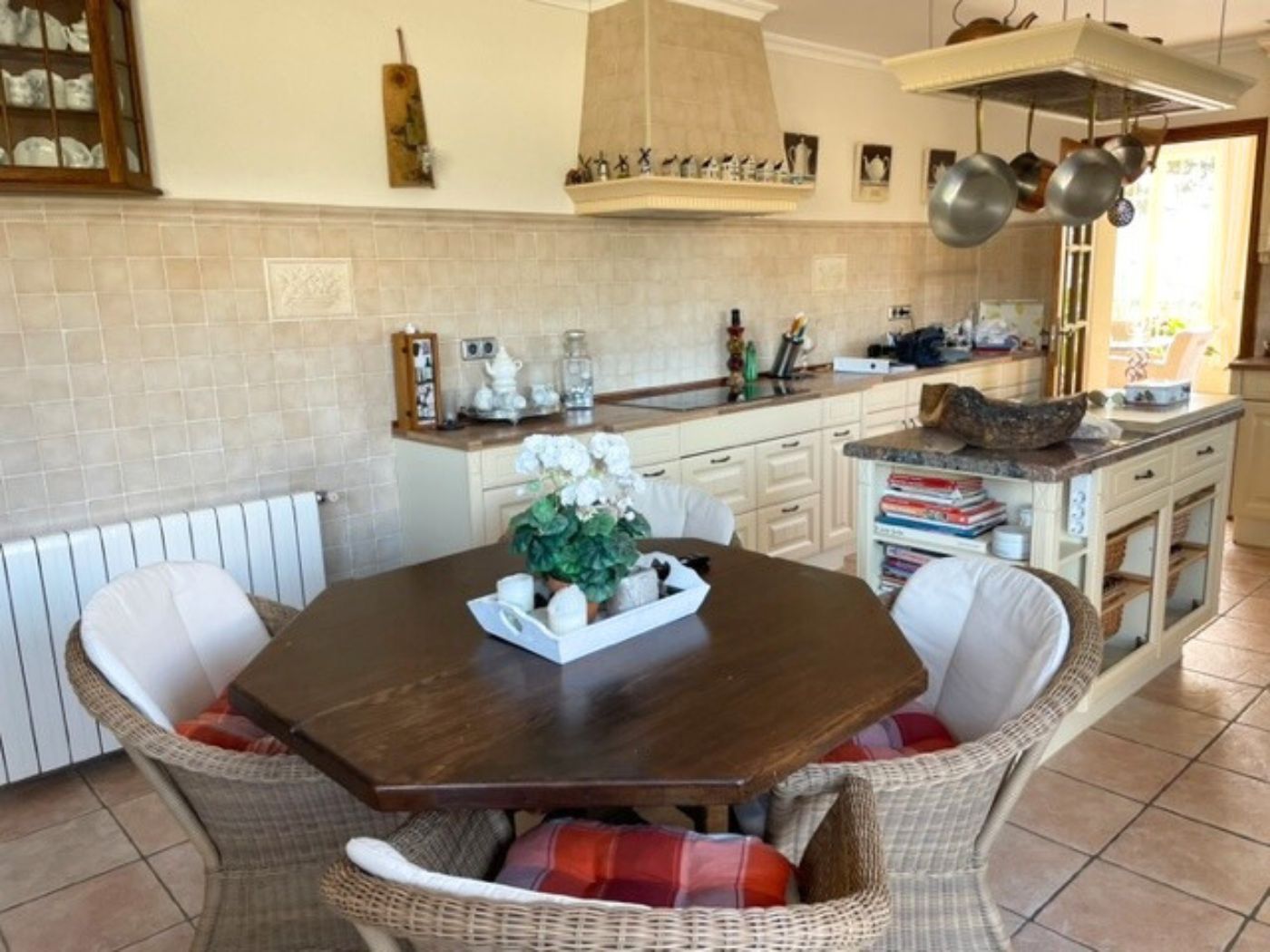 Kitchen featuring an octagonal wooden table with wicker chairs, a central island with a marble countertop, and traditional cream cabinetry with a tiled backsplash.