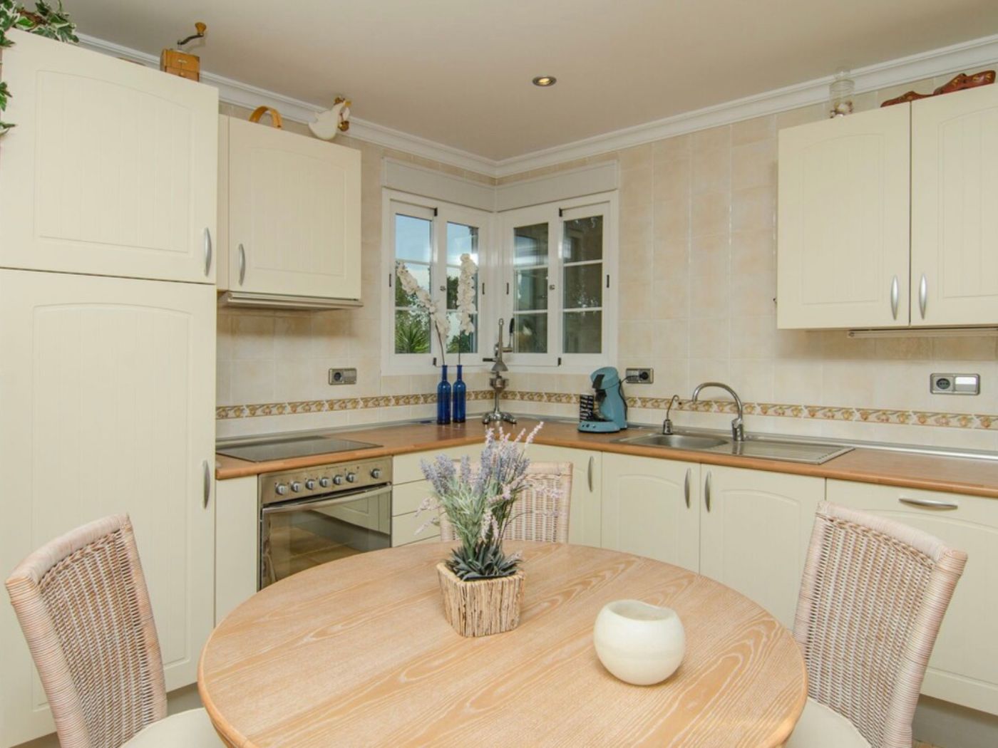 Kitchen featuring cream cabinetry, wooden countertops, and a round dining table with wicker chairs, set against tiled walls with a corner window.